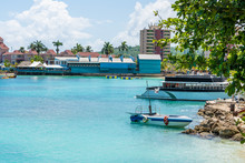 Scenic Sunny Caribbean Landscape View With People Enjoying Water Trampolines, Tour Boats Docked In The Ocean And Seaside Buildings/high Rises In Background On The Coast Of Tropical Ocho Rios, Jamaica.