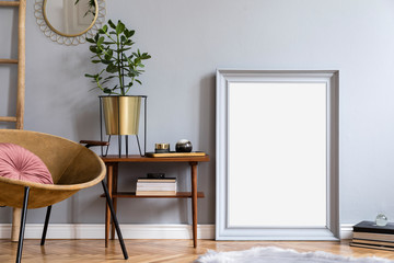 Stylish and luxury interior with design honey yellow armchair, gray mock up frame, gold mirror, wooden ladder. Retro small table with elegant accessories and books. Modern home decor of living room