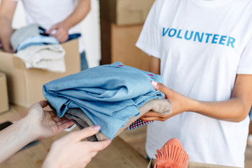 Wall Mural - cropped view of volunteer giving clothes to woman in charity center