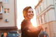 © alones - Portrait of a cheerful joyful beautiful young woman with a cute smile in fashionable black clothes outdoors in the city on a bright sunny day. Positive funny girl model enjoys an orange sunset. Enjoy.