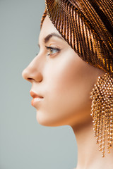 Wall Mural - profile of young woman with shiny make up, turban and golden earring isolated on grey