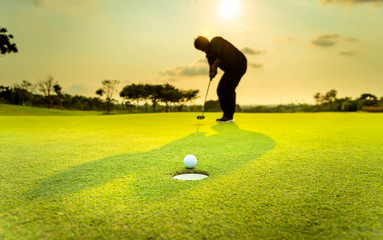 Silhouette golfer showing happiness when win in game , white golf ball on green grass of golf course with blur background.