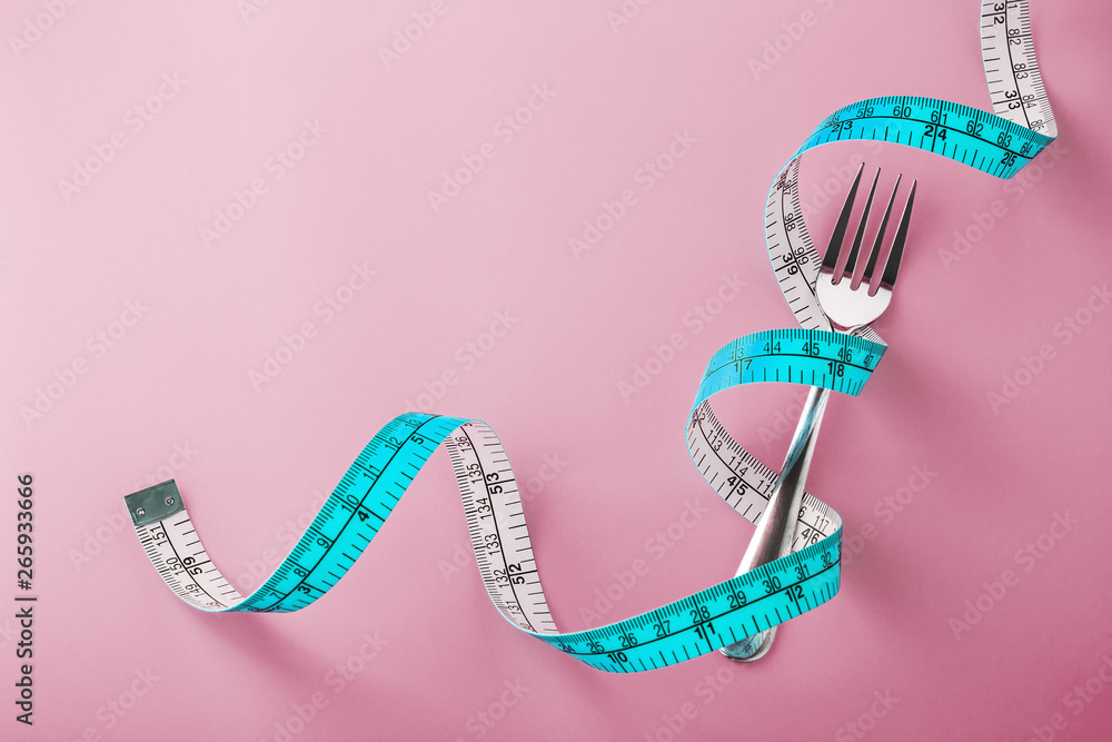 Fork with measuring tape around on pink background - obrazy, fototapety, plakaty 