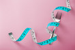 Fork with measuring tape around on pink background