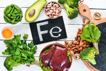 Food containing natural iron. Fe: Liver, avocado, broccoli, spinach, parsley, beans, nuts, on a white wooden background. Top view.