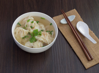 Shrimp wonton in hot soup in white bowl on dark wooden table, Asia food