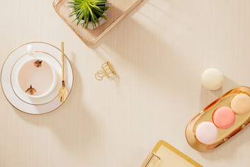 Sticker - Modern gold stylized home office desk with folder, macaroons, coffee mug on beige background. Flat lay, top view lifestyle concept.