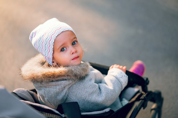 The little girl turns back sitting in a baby carriage on a walk in the park.