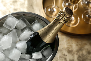 Bottle of champagne in bucket with ice cubes on table, closeup