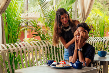 woman closing eyes of his boylfriend to make surprise in restaurant summer tropical cafe urban beach Valentine's Day February 14