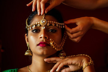 Wall Mural - indian beautiful female in golden rich jewelery and tradition saree face closeup professional make-up wearing bindi on head .Artist doing to muslimgirl with bindis maang tikka ,nath,nose Pin