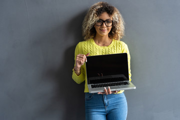 Smiling casual woman showing laptop screen over gray background. Looking at camera.