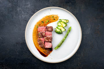 Barbecue dry aged wagyu fillet steak on hot smoked sauce with grilled green asparagus and sliced zucchini as top view on a modern design plate with copy space