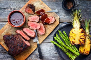 Wall Mural - Barbecue dry aged wagyu tri tip steak with grilled pineapples and green asparagus top view on a wooden cutting board