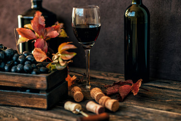 Wall Mural - Red wine tasting in the winery. Full wine glass next to a vintage box and lush vine leaves on the background, winemaking concept. Toned image. Selective focus.