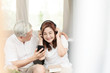 © ChayTee - Candid of attractive older couple asian sitting relax together on couch at home in lifestyle of retirement people concept. Asian old man and senior woman listen to music on podcast from mobile phone.