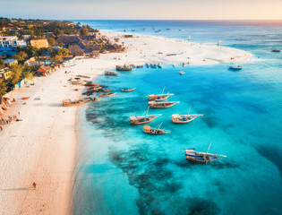 Wall Mural - Aerial view of the fishing boats on tropical sea coast with sandy beach at sunset. Summer holiday on Indian Ocean, Zanzibar, Africa. Landscape with boat, buildings, transparent blue water. Top view