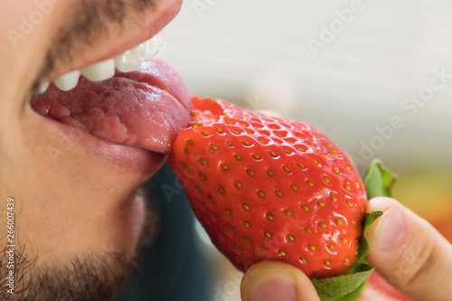 Fotografía A young man bites and licks ripe strawberries