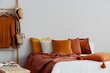 Dirty orange pillows on bed in stylish bedroom with copy space on empty wall