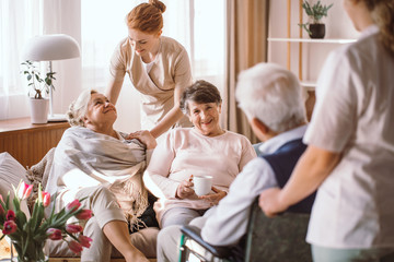 Wall Mural - Young caregiver comforting elderly woman in nursing home