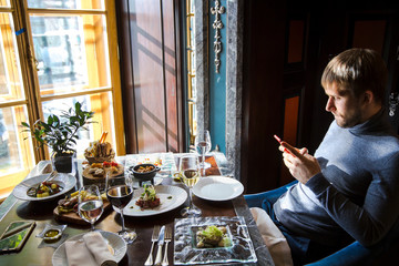 Business lunch. Contemporary young man in elegant restaurant using cell phone to type a text message.