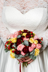 Wall Mural - Luxurious bouquet of pink, red and yellow roses in the hands of an unrecognizable bride