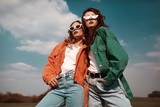 Fototapeta Tulipany - High fashion portrait of two stylish beautiful woman in trendy jackets and jeans posing outdoor. Vogue style.