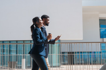 Canvas Print - Business people walking and carrying tablet and drink outdoors. Business man and woman wearing formal clothes with building in background. Business people and break concept. Side view.