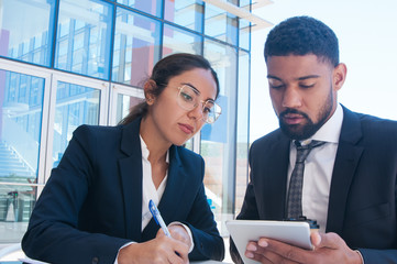 Canvas Print - Business people working and using tablet in outdoor cafe. Business man and woman wearing formal clothes and sitting with building glass wall in background. Business work concept. Front view.