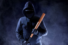 A Man With A Hood Is Standing In The Dark. He Is Armed With A Baseball Bat. Concept Violence.