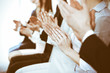 © rogerphoto - Business people clapping and applause at meeting or conference, close-up of hands. Group of unknown businessmen and women in modern white office. Success teamwork or corporate coaching concept
