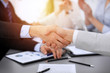 © rogerphoto - Business people shaking hands at meeting while theirs colleagues clapping and applauding. Group of unknown businessmen and women in modern white office. Success teamwork, partnership and handshake
