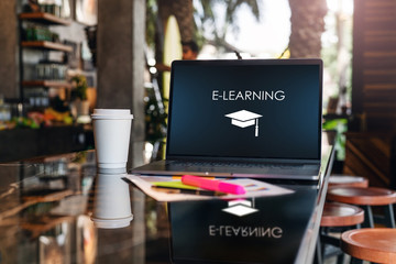 Close up of laptop with inscription on screen e-learning on table in empty room, cafe. Distance learning. Online education.