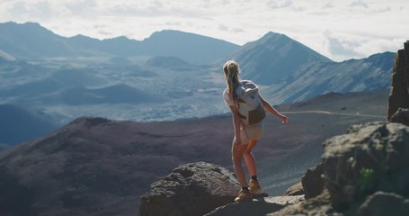 young adventurous woman leaps onto a rock in slow motion and enjoys the view from the top of a mount