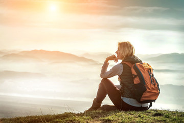 Happy woman tourist sitting on the green grass on the peak of mo