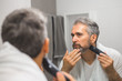 © cherryandbees - middle aged bearded gray haired man trimming his beard in bathroom