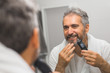 © cherryandbees - middle aged bearded gray haired man trimming his beard in bathroom