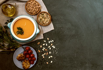 Wall Mural - Traditional fall dishes, hot and spicy pumpkin soup with pumpkin seeds and cream on gray stone table. Autumn dinner. Organic vegetables and healthy food concept. Top view with copy space. Toned image