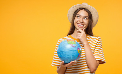 Young female dreaming about future trip, holding globe with one hand, isolated on yellow background. Travel concept.