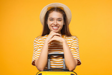 Excited young woman tourist with beautiful smile and suitcase, isolated on yellow background