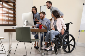 Canvas Print - Young woman in wheelchair with colleagues at workplace