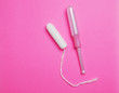 Woman Hygienic tampons with applicator on pink backdrop surface.