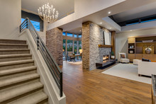 Spacious New Luxury Home Interior In Luxury Home With Large Stone Fireplace, Roaring Fire, View Of Den And Staircase.