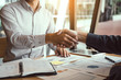 © wutzkoh - Entrepreneurs collaboration deal shaking hands in a modern office and financial paper graph on desk.