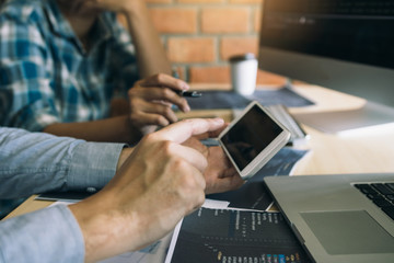 Software developers are using smart phones and analyzing together the code written in the program on the computer.
