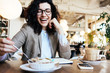 Portrait of pretty smiling business lady sitting in eco cafe with notepad, phone, cup of coffee, eating tasty desert
