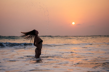 Wall Mural - young woman in sexy swimming suit black thong in sea wawes having fun at sunset Goa beach India ocean