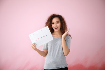 Wall Mural - African-American woman holding calendar with marked days of menstruation on color background