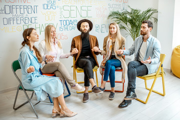 Wall Mural - Young people holding hands together during the psychological therapy, meditating and solving together some mental problems in the office