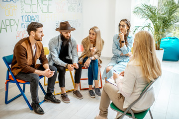 Wall Mural - Group of young people sitting together during the psychological therapy with psychologist solving some mental problems in the office